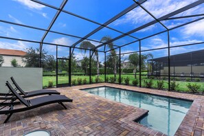 A swimming pool with a brick patio and lounge chairs, surrounded by a glass enclosure.