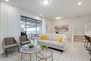 Uma sala de estar moderna com um sofá, poltronas, uma mesa de centro de vidro e uma escada.