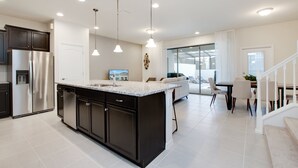A modern kitchen with dark cabinetry, a large island, and pendant lighting. - 5 bed Town Home With Pool (Kissimmee)