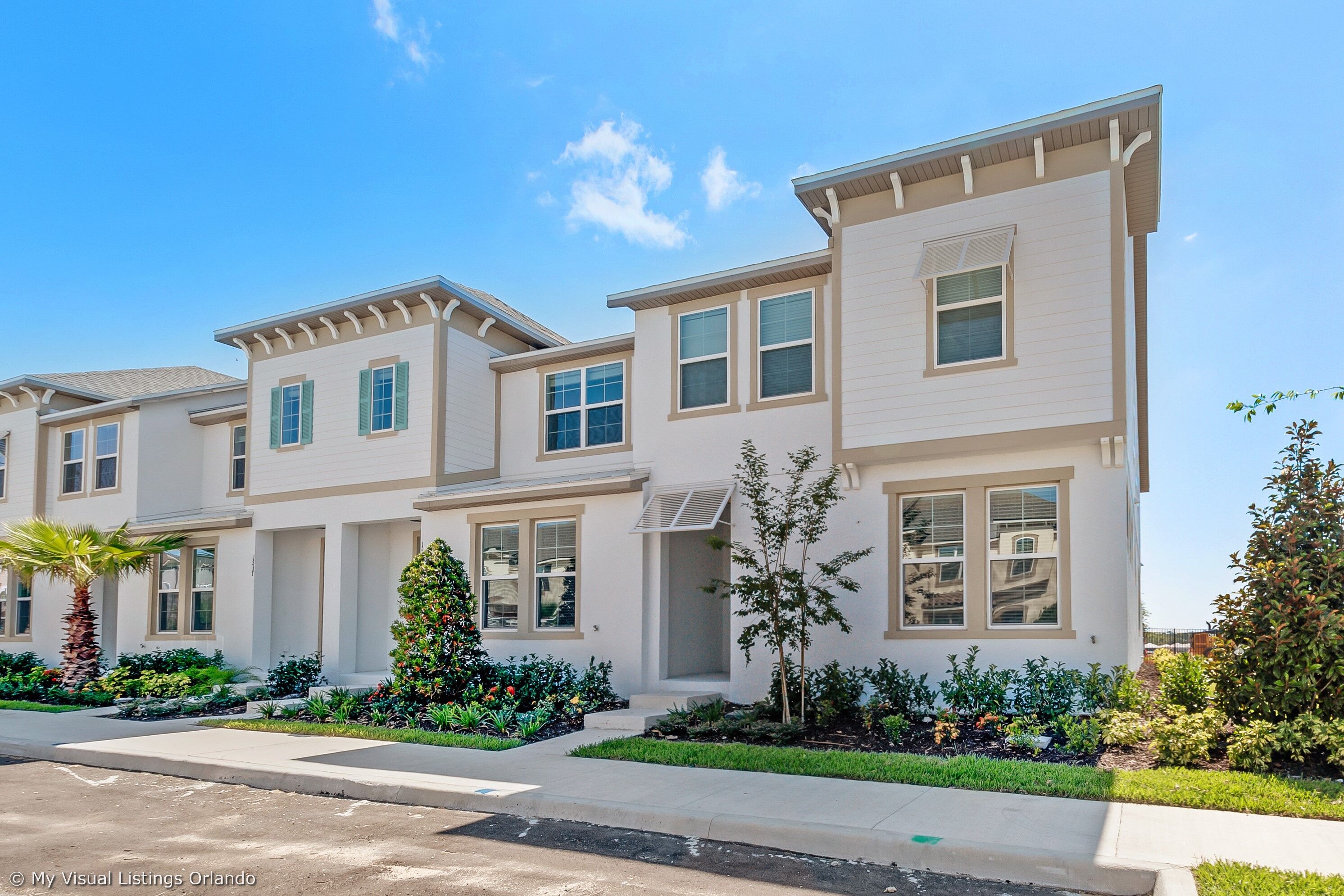 A modern multi-story residential building with a symmetrical facade, large windows, and a well-maintained front yard with landscaping.