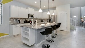 A modern kitchen with white cabinets, a granite countertop, stainless steel appliances, and a central island with bar stools. - 8917bengal Sleeps 20 (Kissimmee)