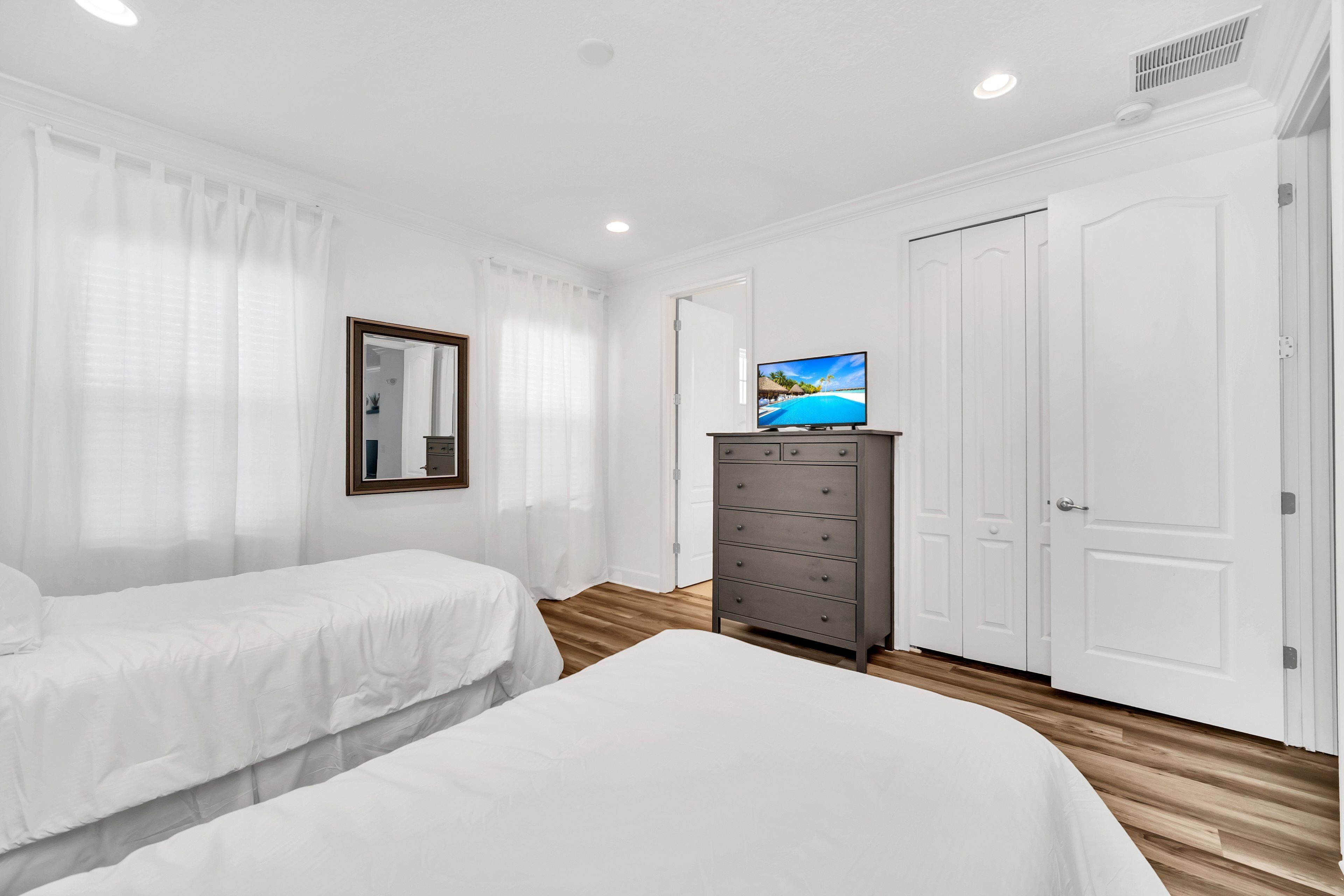Habitación de hotel con dos camas, un tocador, un televisor y paredes blancas.