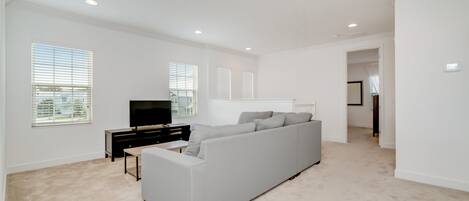 Un salón amplio con un sofá modular gris grande, un televisor de pantalla plana y una pequeña mesa de centro.