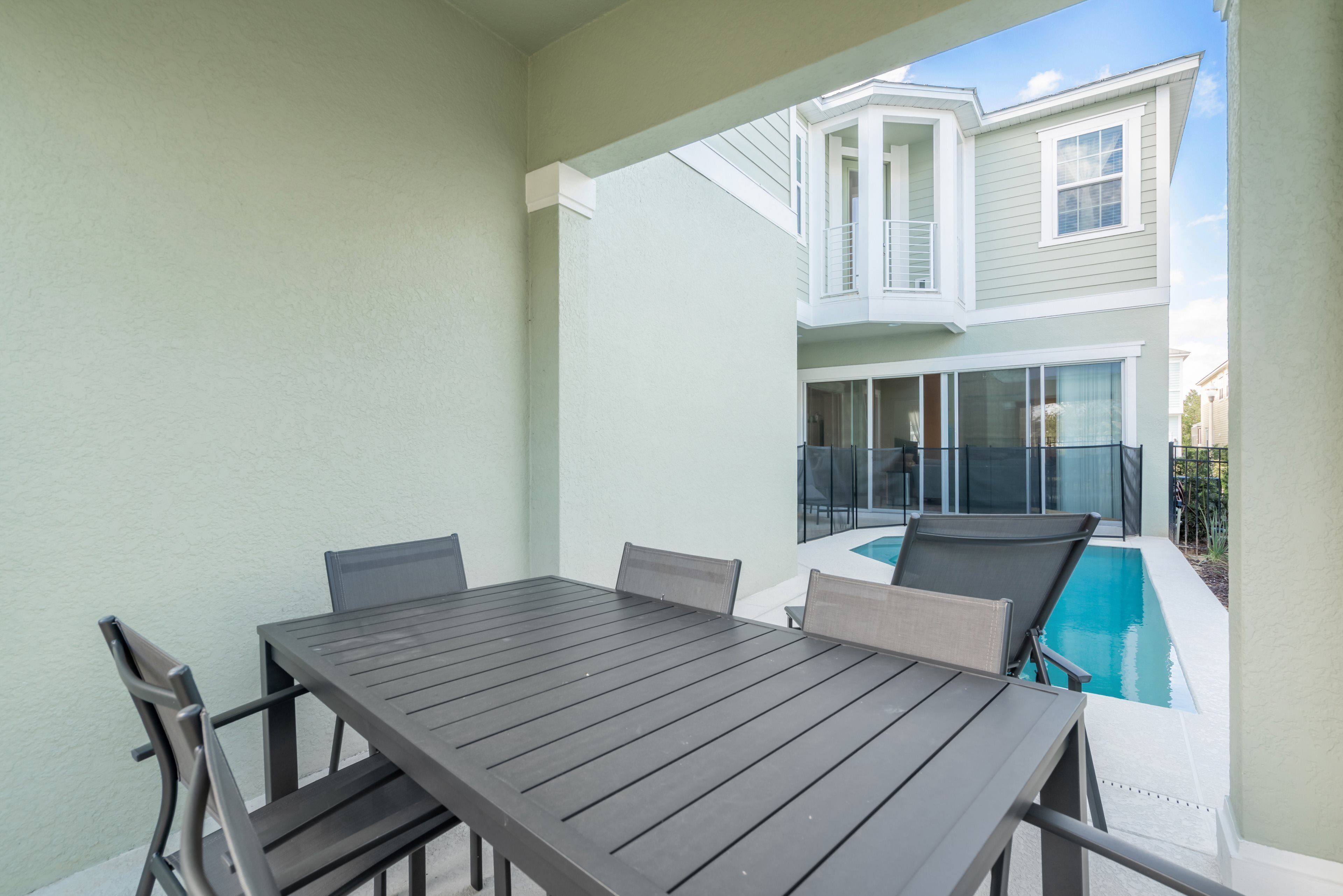 A patio with a table and chairs, a pool, and a house in the background.