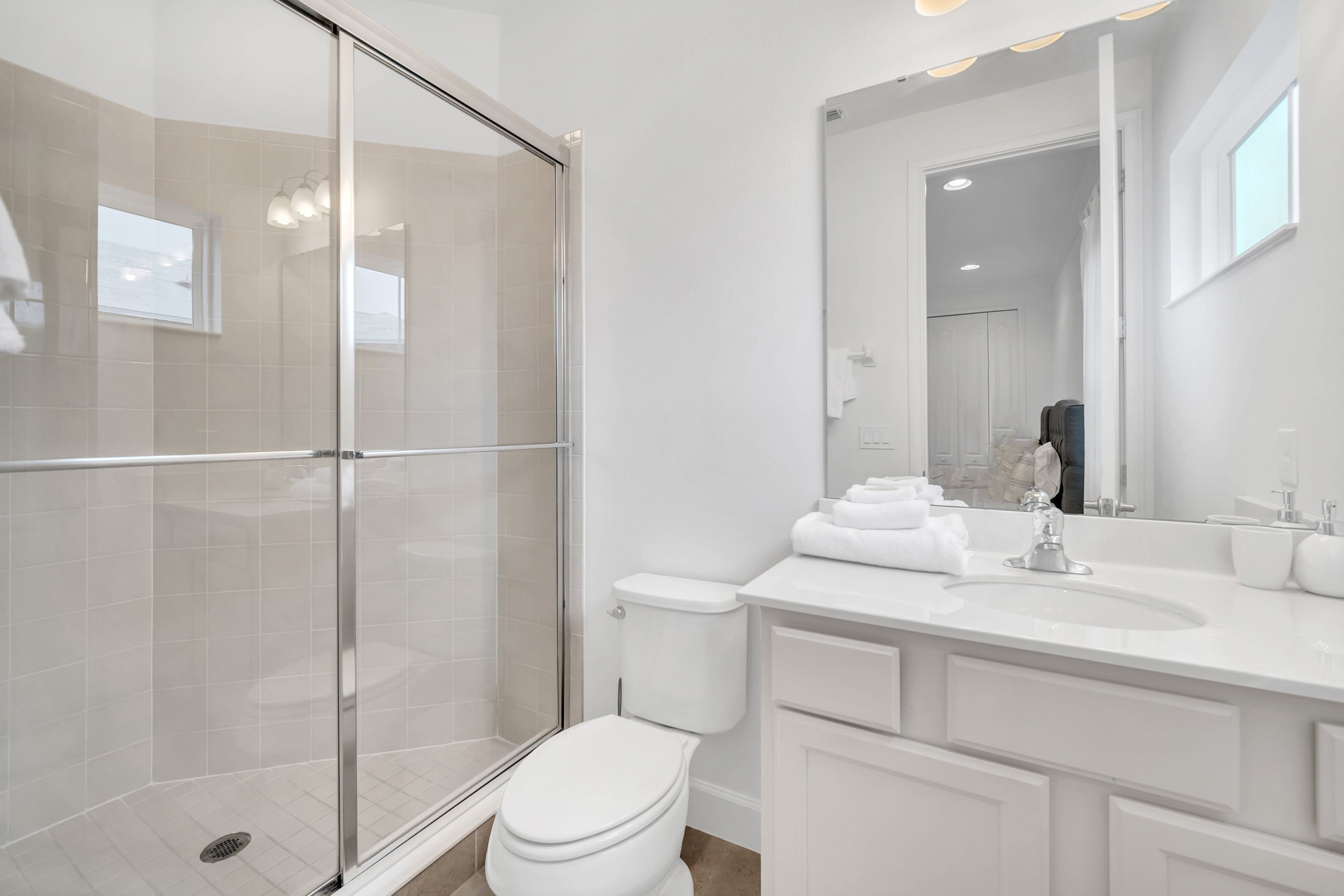A modern bathroom with a glass shower enclosure, a white toilet, and a large mirror above a white sink.