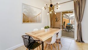 A dining area with a wooden table, white chairs, a black chair, a hanging light fixture, and a framed picture on the wall. - 8929bismark (Kissimmee)
