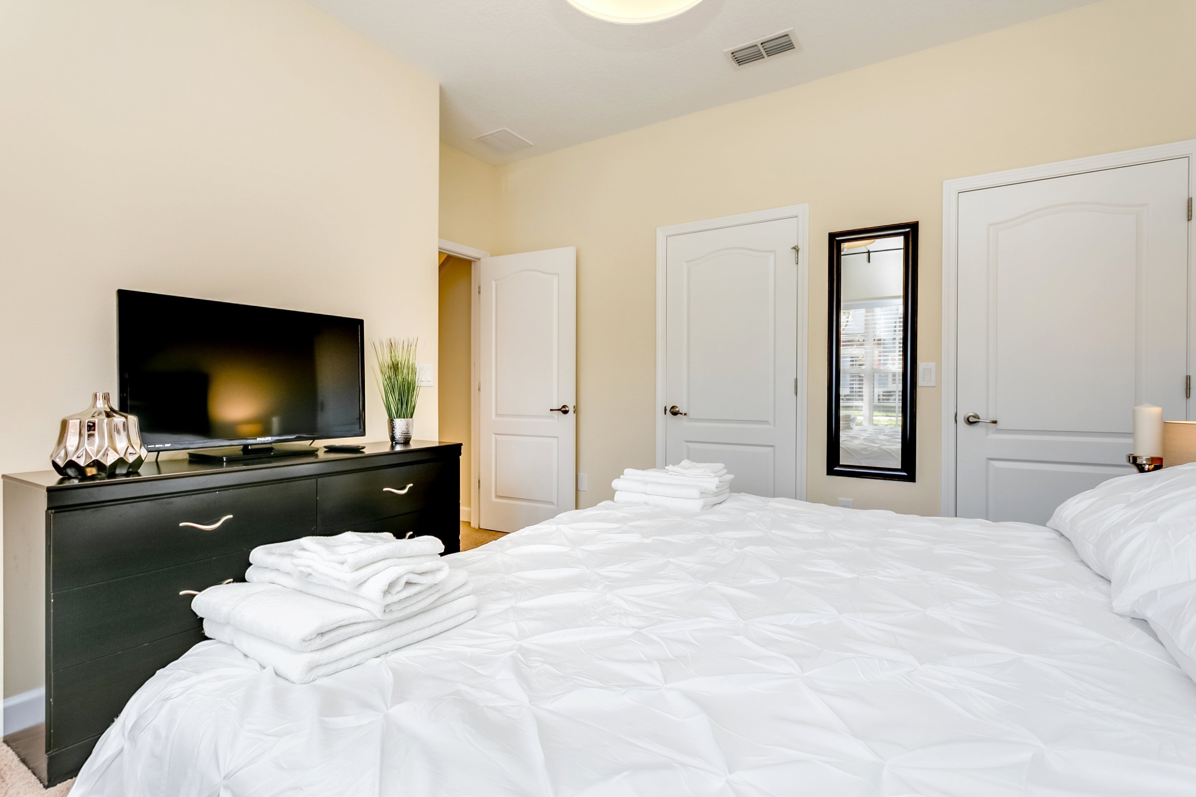 A bedroom with a large bed, a dresser, a television, and two doors.