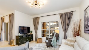 A modern living room with a flat-screen TV, a sofa, a coffee table, and a large window with curtains. - 8929bismark (Kissimmee)