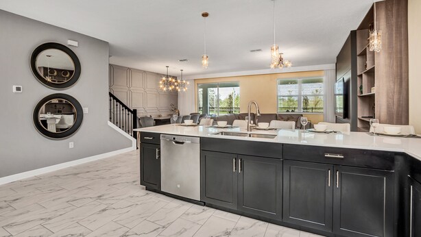 A modern kitchen with a large island, dark cabinetry, and a central island sink. There are two round mirrors on the wall, a staircase leading to another level, and pendant lighting. - 9 Bedroom Champions Gate Villa (Kissimmee)