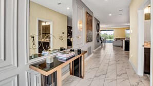 A spacious hallway with a marble floor, a console table with books and trophies, and a large mirror reflecting the room. - 9 Bedroom Champions Gate Villa (Kissimmee)