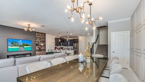 A modern kitchen with dark cabinets, a central island, and a dining area with a wooden table and white chairs. - 9 Bedroom Champions Gate Villa (Kissimmee)