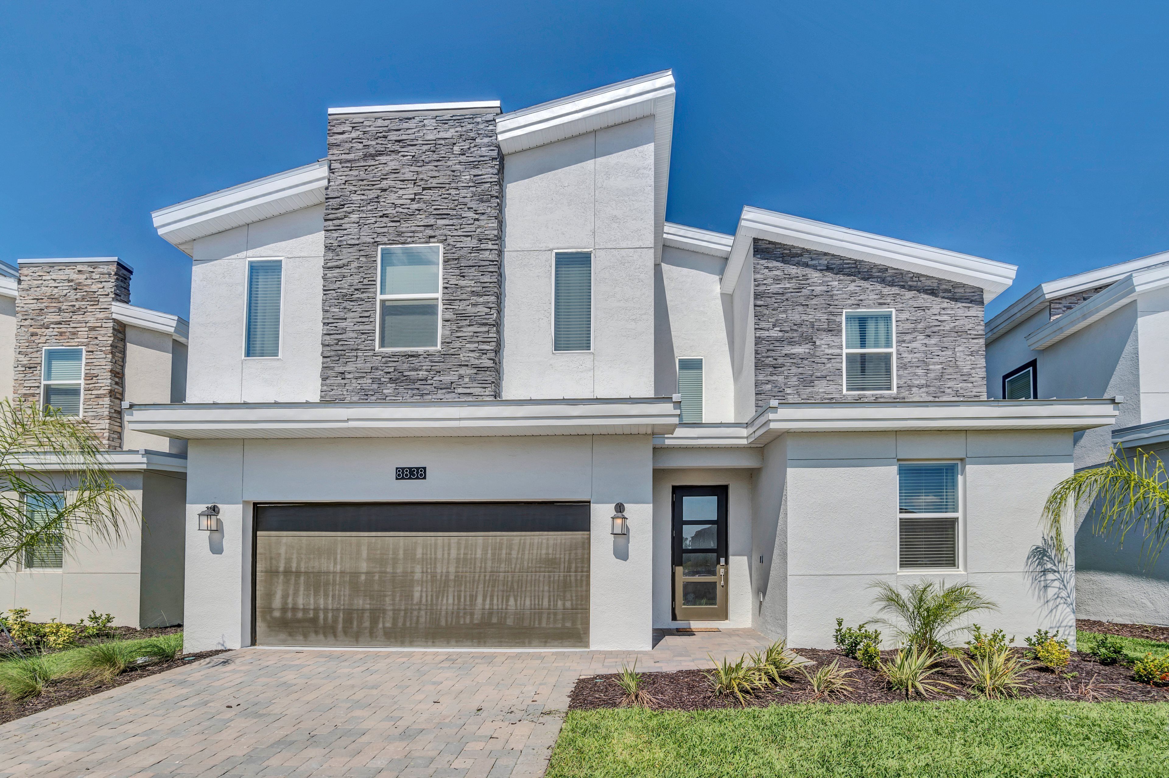 A modern two-story house with a stone facade, a garage, and a well-maintained lawn.