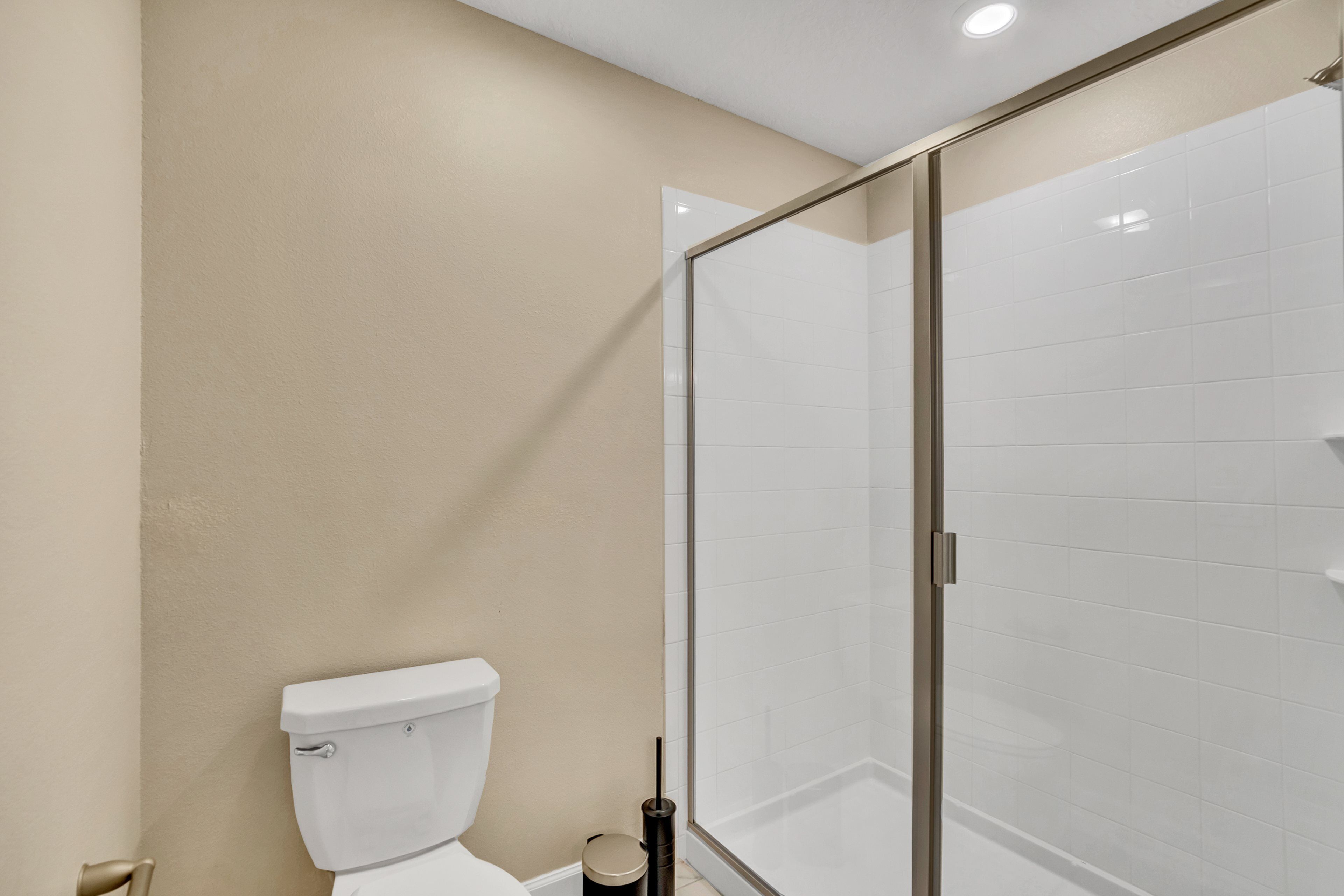 A bathroom with a toilet, a glass shower enclosure, and a beige wall.