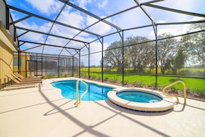 A covered outdoor swimming pool with a hot tub, surrounded by a metal frame and glass walls, overlooking a green landscape. - 5 Bdrm Solterra New Home (Davenport)