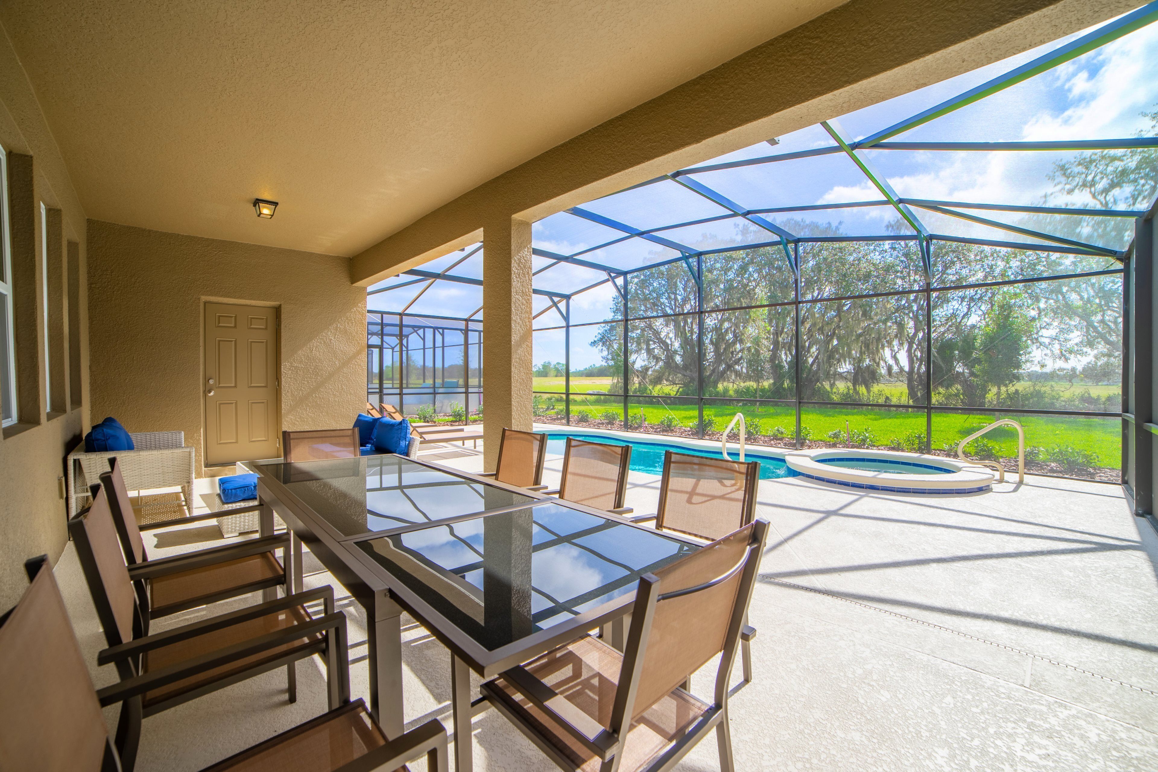 An outdoor patio with a glass-enclosed pool, a dining table with chairs, and a door leading to the interior.
