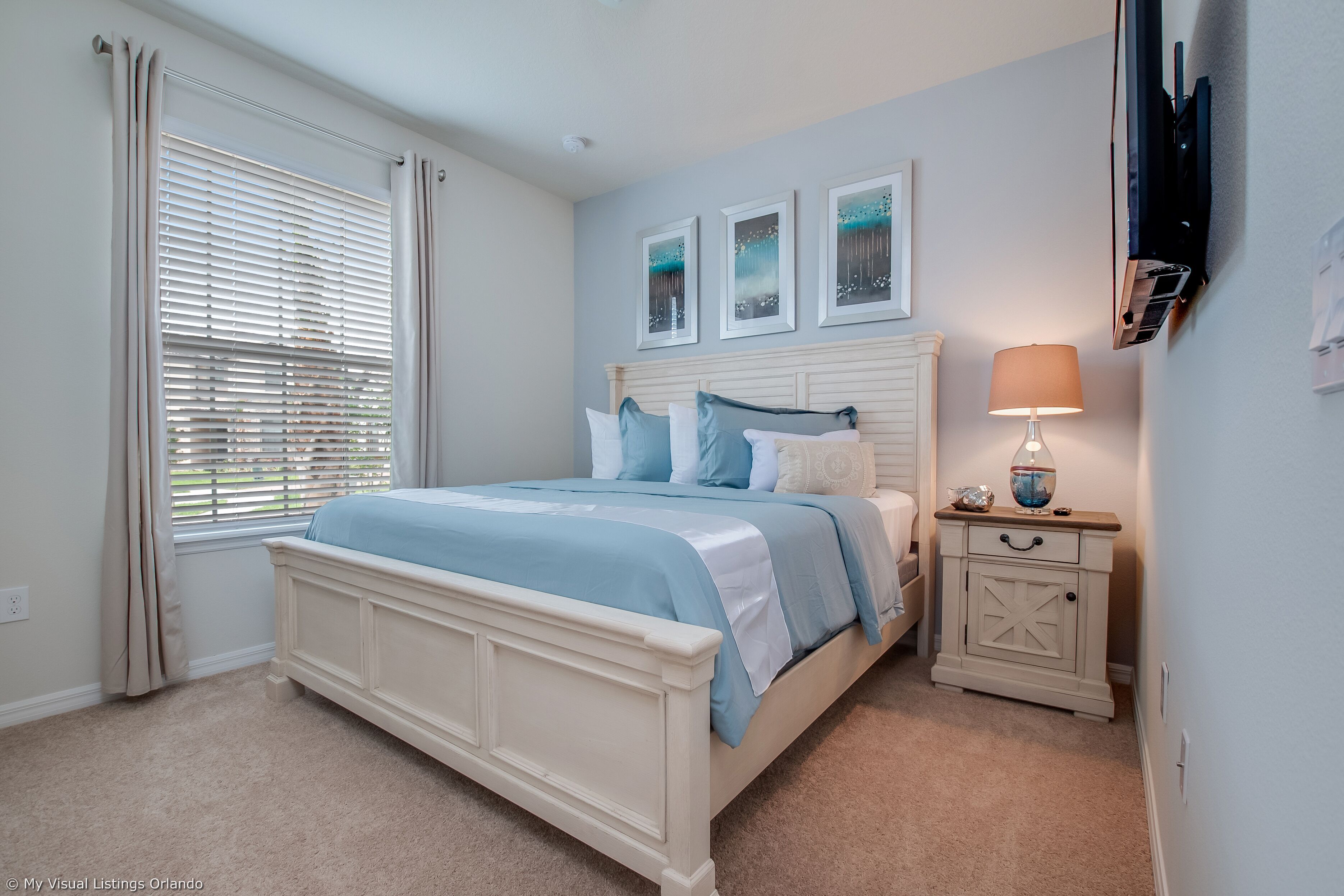 A bedroom with a bed, a nightstand, a lamp, and a TV mounted on the wall.