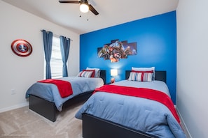 Une chambre avec deux lits, un ventilateur de plafond, un bouclier du Capitaine America et une fresque murale.