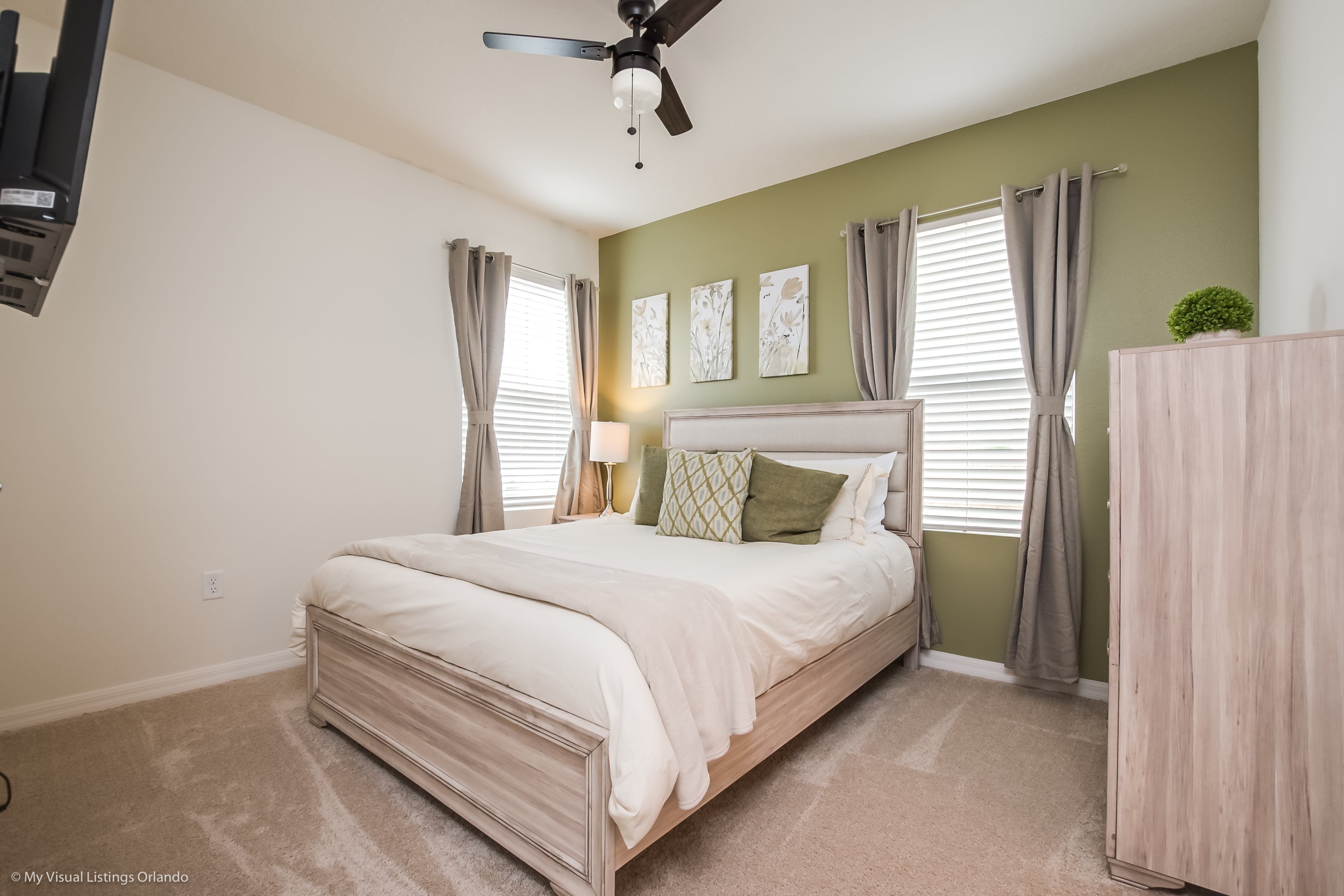 A bedroom with a bed, a ceiling fan, a nightstand with a lamp, and a dresser.