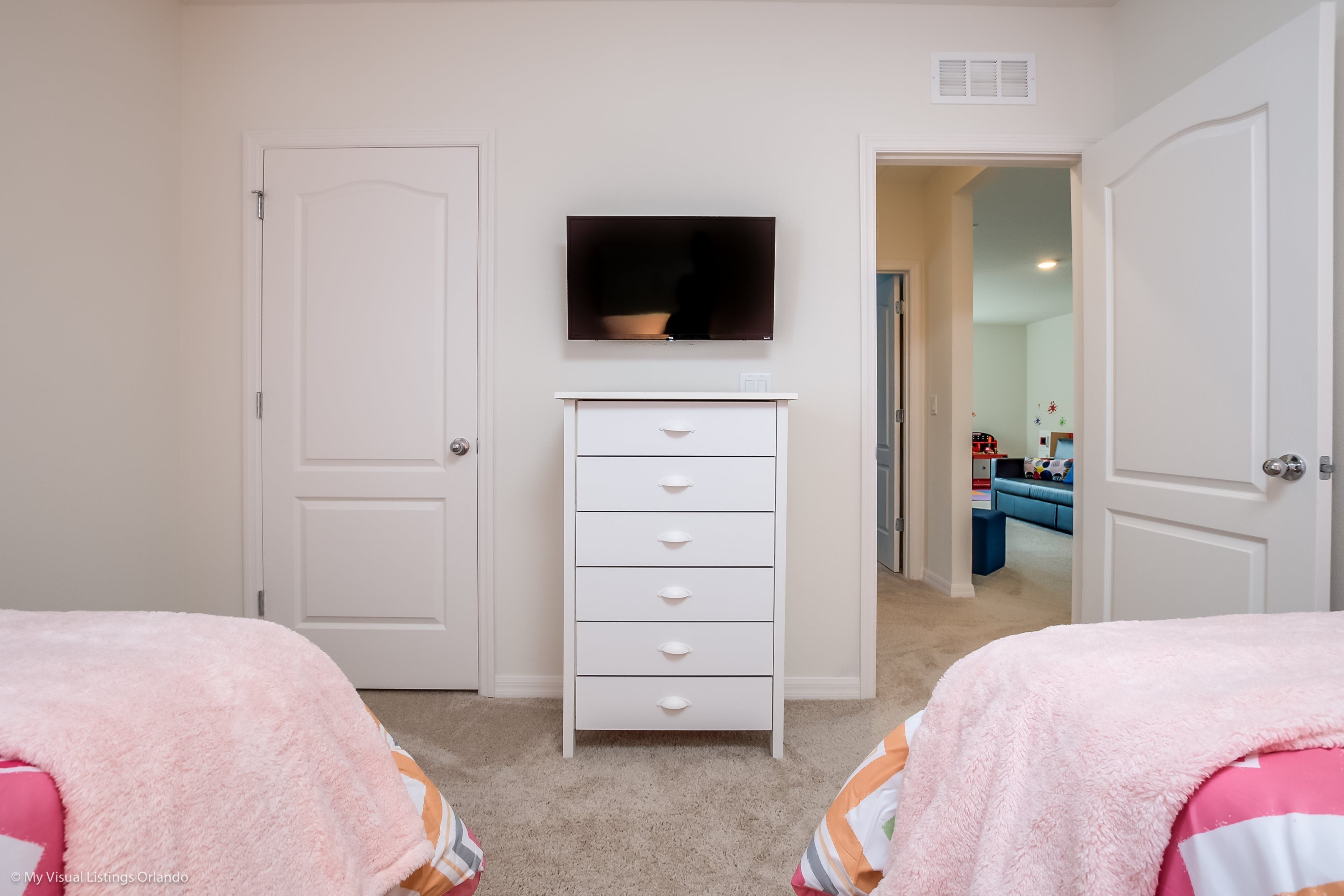 A bedroom with two beds, a white dresser, a television, and a door leading to another room.