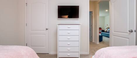A bedroom with two beds, a white dresser, a television, and a door leading to another room.
