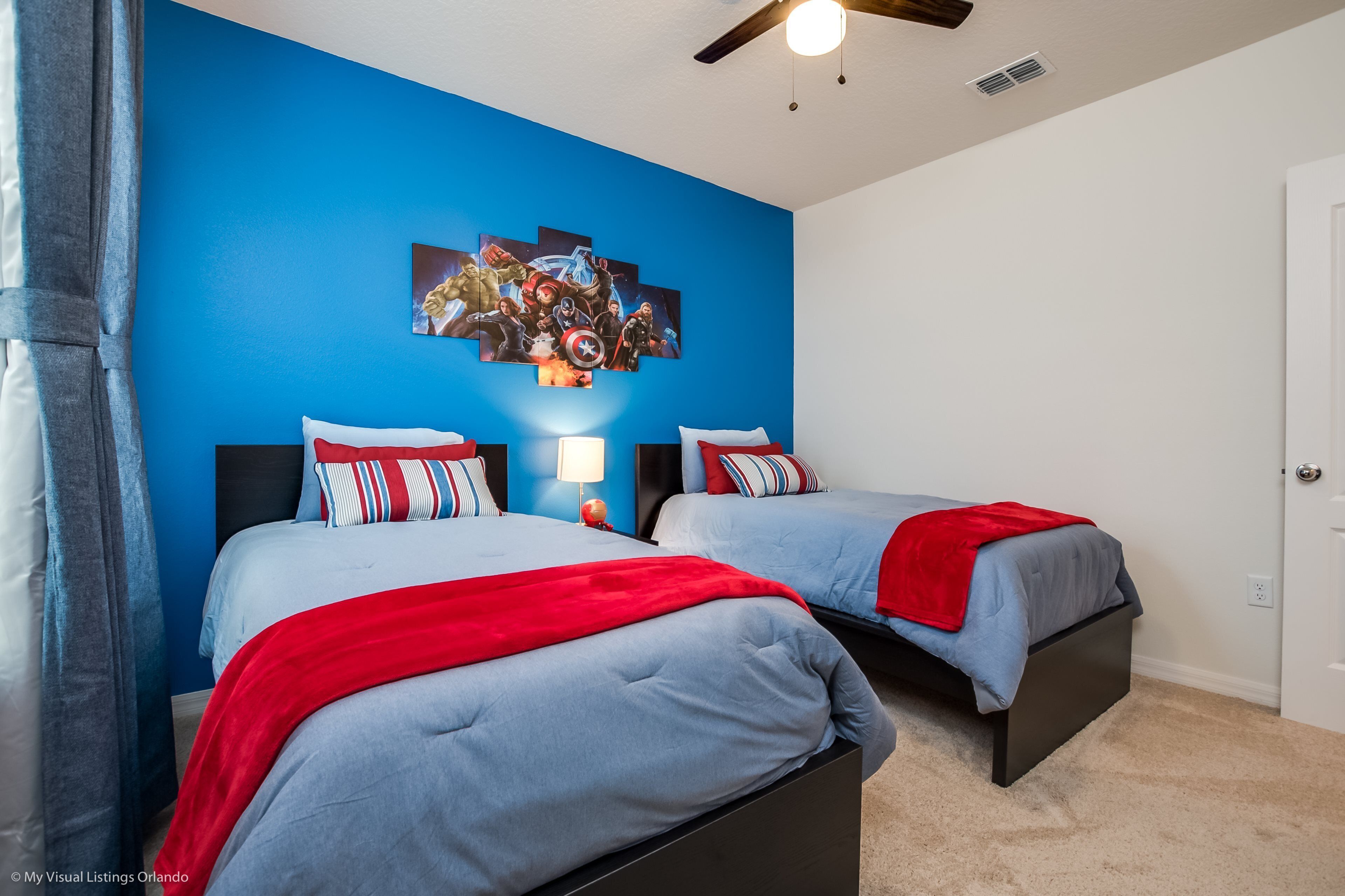 A bedroom with two beds, a blue accent wall, and a ceiling fan.