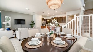 A dining area with a round table set for six, surrounded by white sofas and a TV on the wall. - 1939majorca Fantastic 5 Bed 4 Bathroom Town Home (Kissimmee)