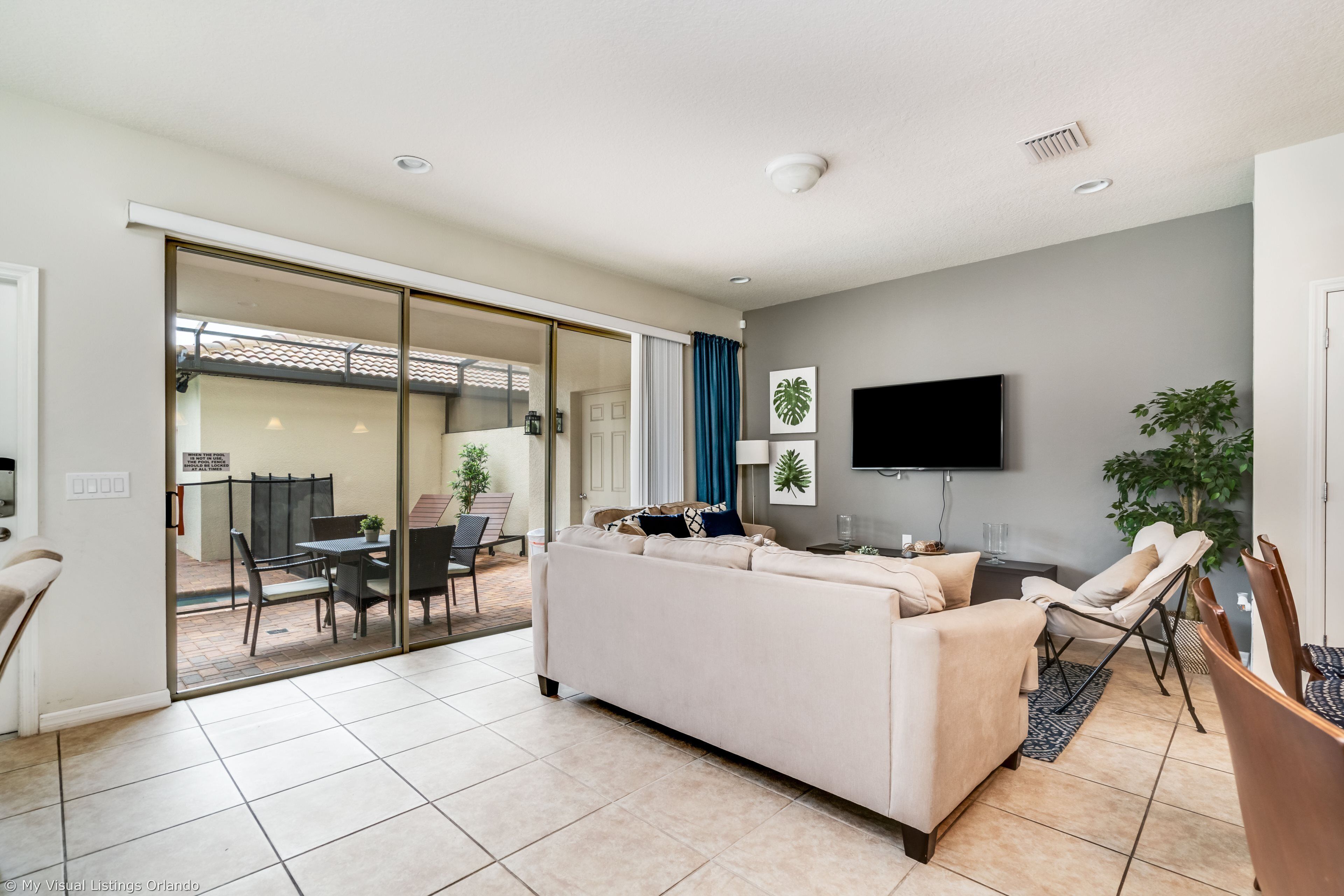 A modern living room with a sofa, TV, and a sliding glass door leading to an outdoor patio.