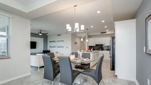 A modern kitchen with white cabinets, a dining area with a glass table and black chairs, and a ceiling fan. - Beautiful 2 Bdrm 2 BA Condo (Kissimmee)