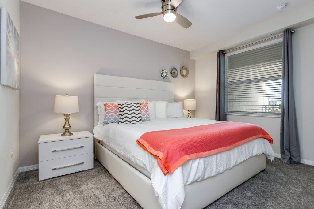 A bedroom with a bed, nightstands, a ceiling fan, and a window with blinds.