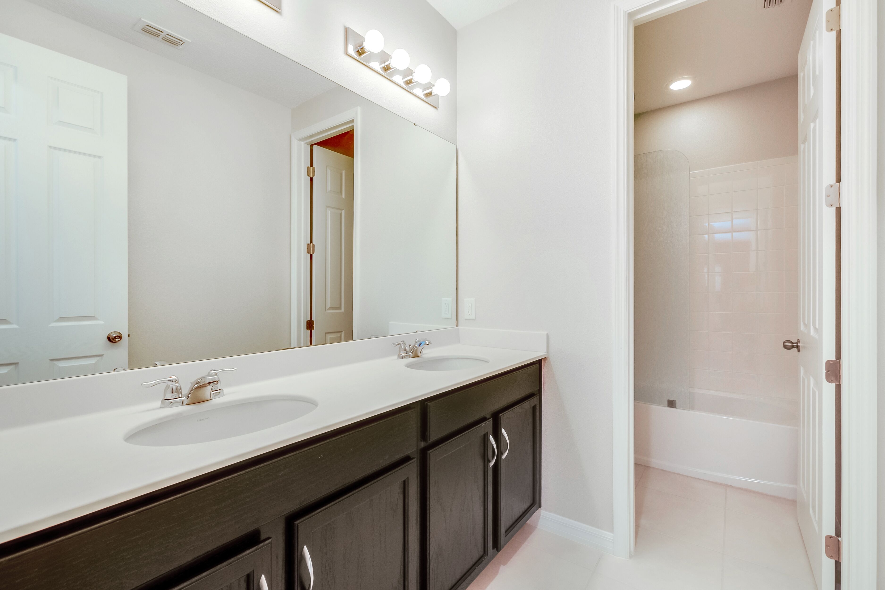 A bathroom with a double sink vanity, a large mirror, and a shower area.