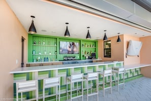 A bar area with green cabinets, multiple hanging lights, and bar stools. - 1773caribbean (Kissimmee)