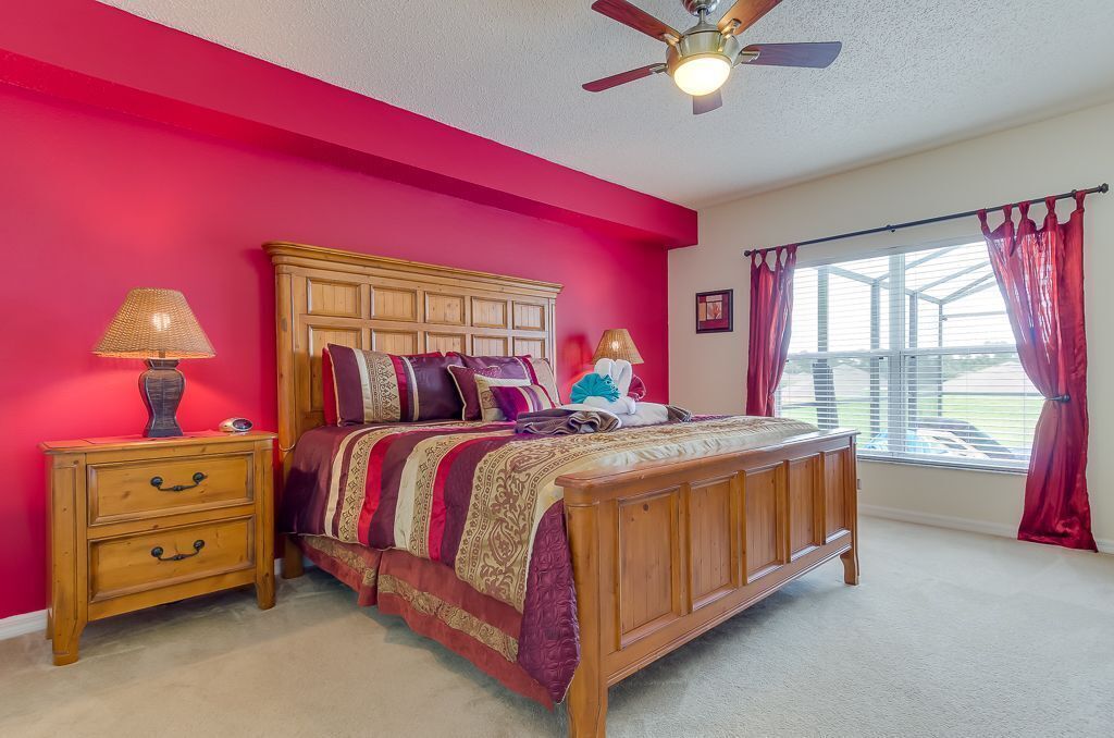 A bedroom with a wooden bed, a nightstand with a lamp, and a window with curtains.