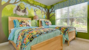 Une chambre d’enfant avec deux lits, une fresque murale et une fenêtre avec des stores.