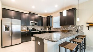 A modern kitchen with dark cabinetry, stainless steel appliances, a granite countertop, and bar stools. - 6 Bedroom, 6 Bath Pool Home (Davenport)