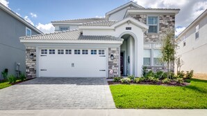 A modern two-story house with a white garage door, stone facade, and a well-maintained lawn. - 6 Bedroom, 6 Bath Pool Home (Davenport)