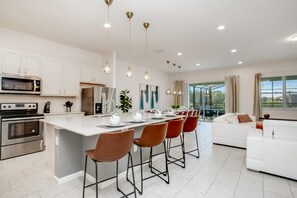 A modern kitchen with white cabinets, stainless steel appliances, and a central island with bar stools. - 6052broa (Davenport)