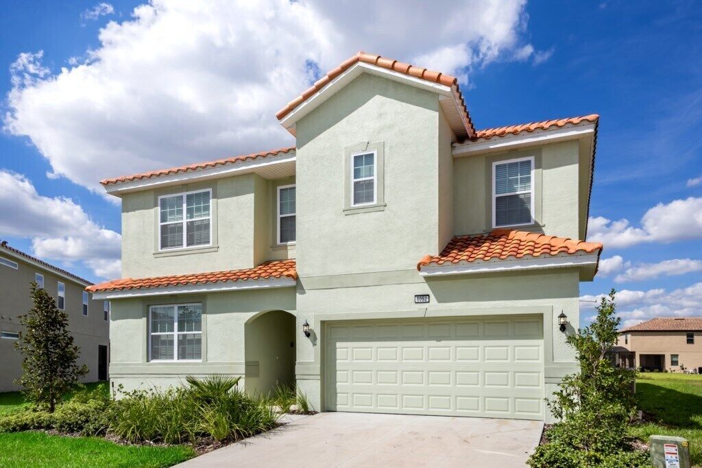 A two-story residential building with a light green exterior, a red-tiled roof, and a garage.