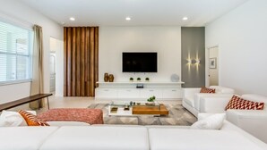 A modern living room with a white sofa set, a glass coffee table, and a flat-screen TV mounted on the wall. - 6052broa (Davenport)