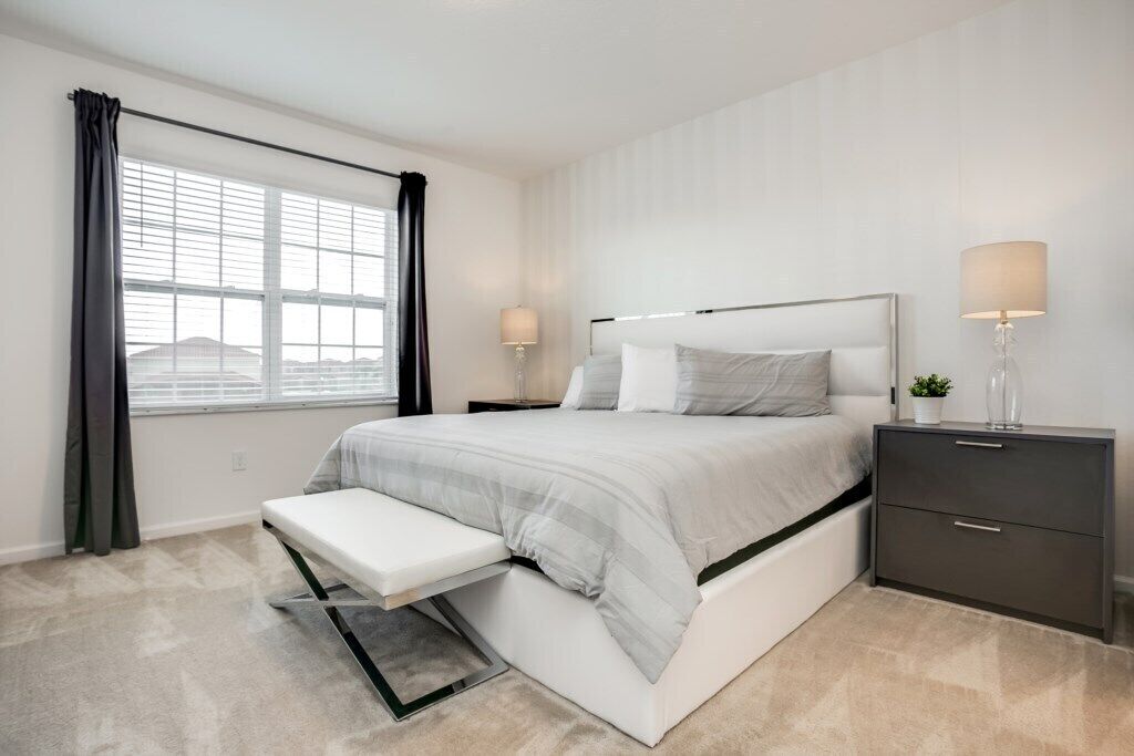Une chambre à coucher moderne avec un grand lit, des tables de chevet, un banc et une fenêtre avec des rideaux.
