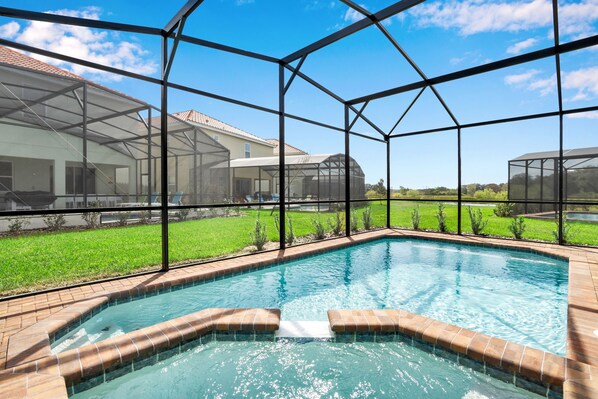A swimming pool with a glass enclosure, surrounded by a grassy area and a house.