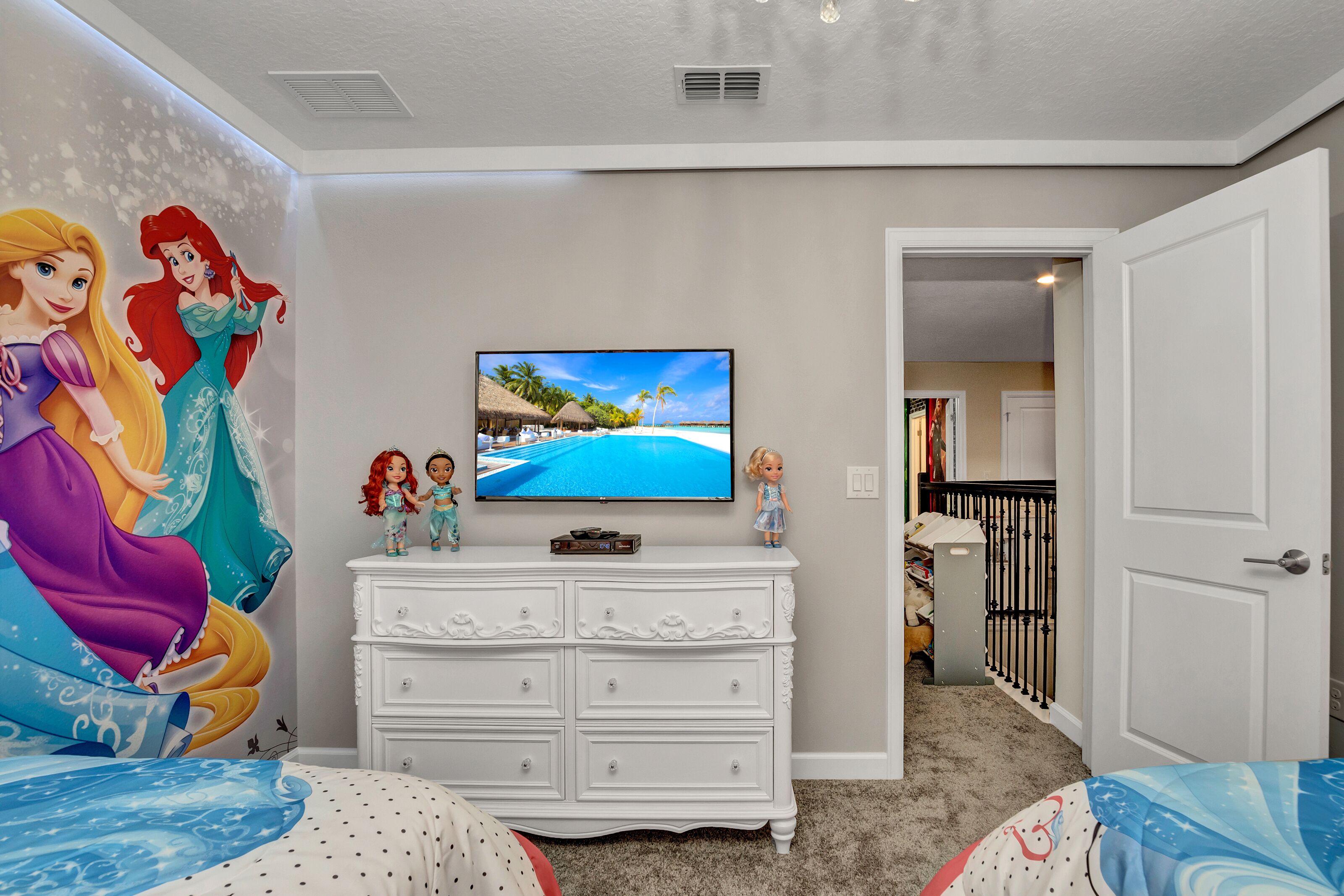 A bedroom with a TV, a dresser, and a mural of Disney princesses.