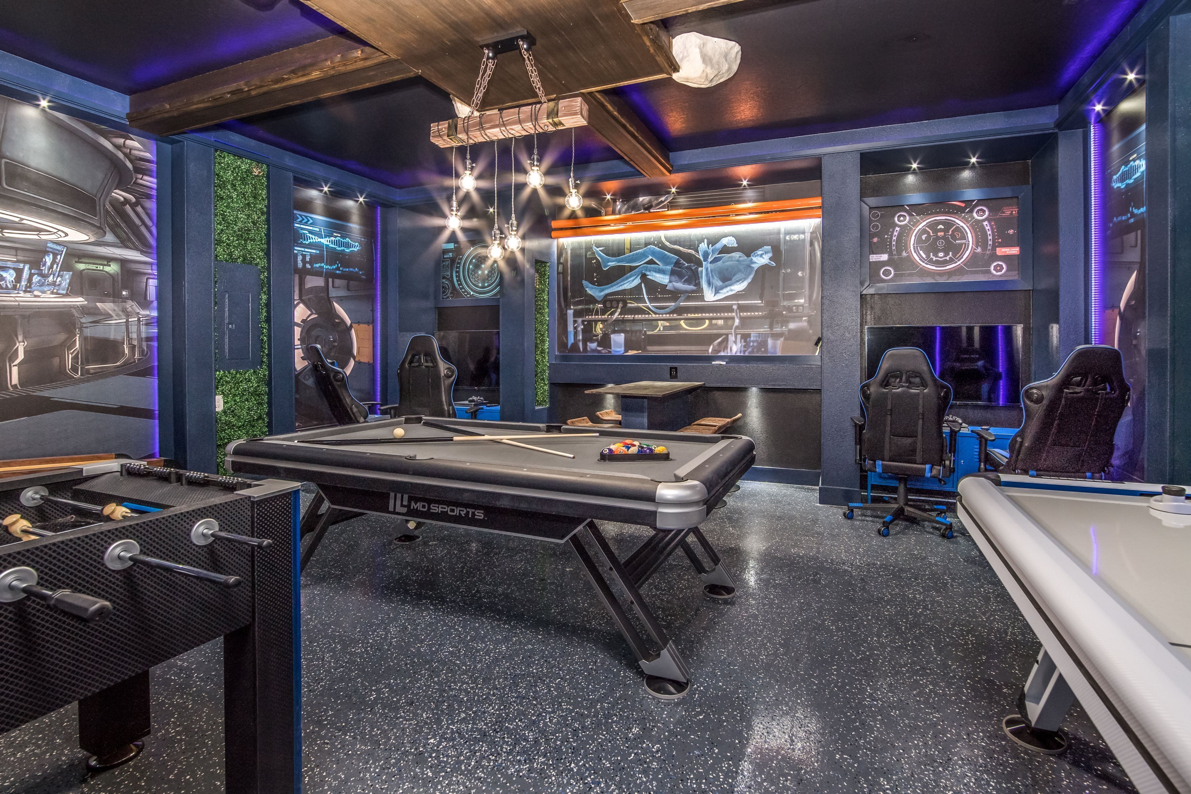 A pool table with a foosball table, a billiards table, and a bar area with a neon sign.