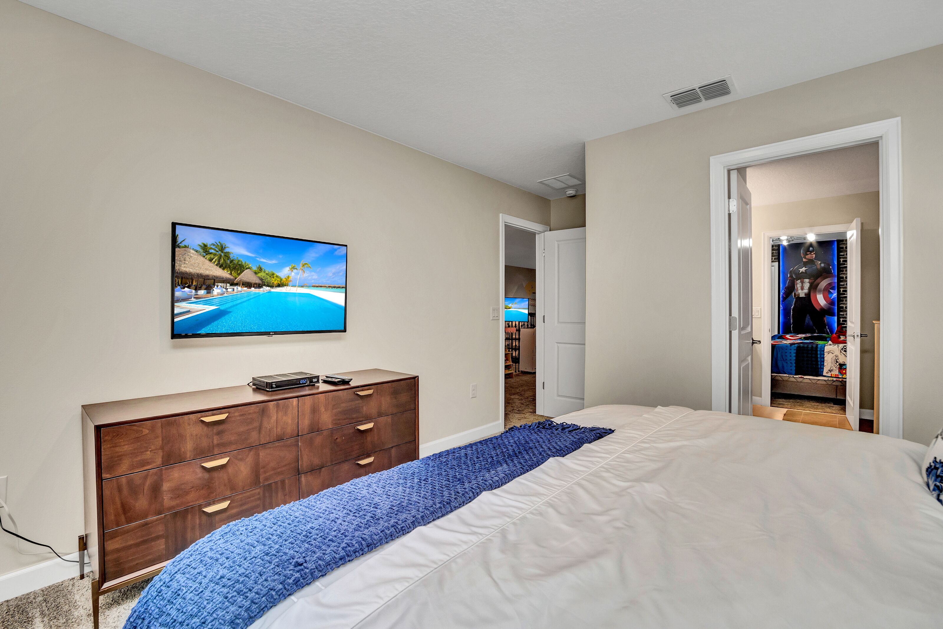A bedroom with a bed, a dresser, a TV on the wall, and a closet.