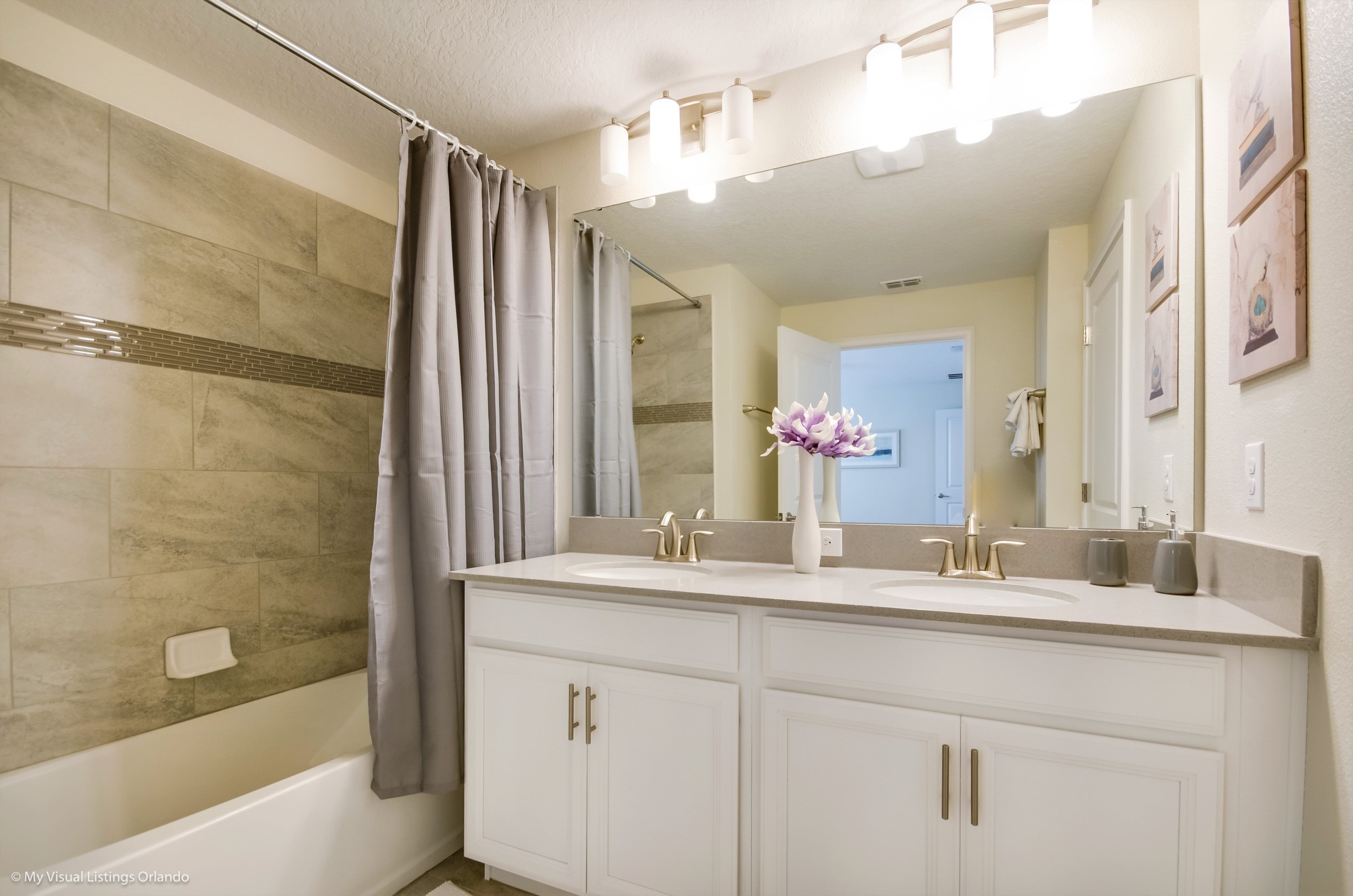 A bathroom with two sinks, a shower, and a vanity with cabinets.