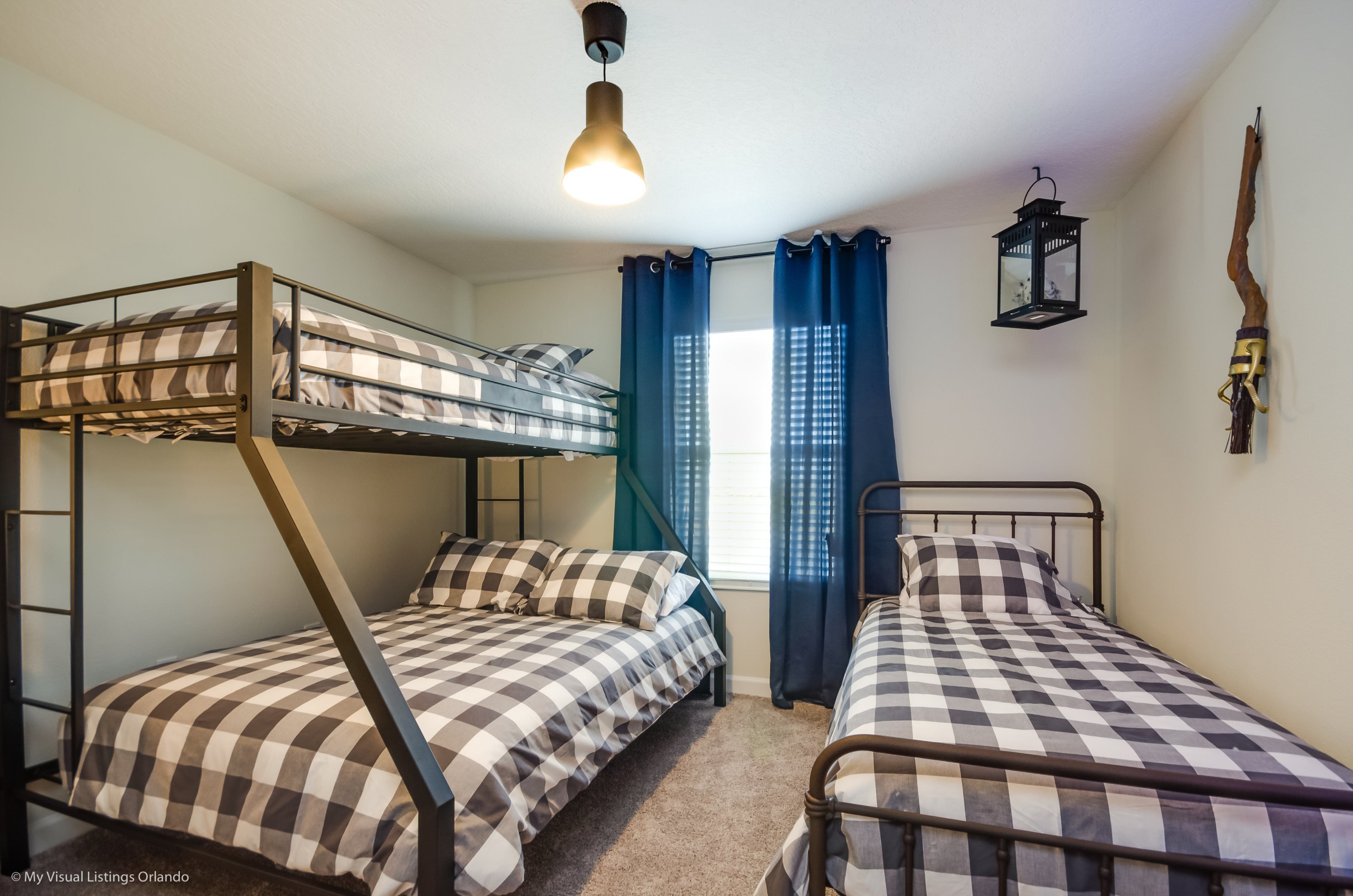 A dormitory room with bunk beds, a hanging lantern, and a window with curtains.