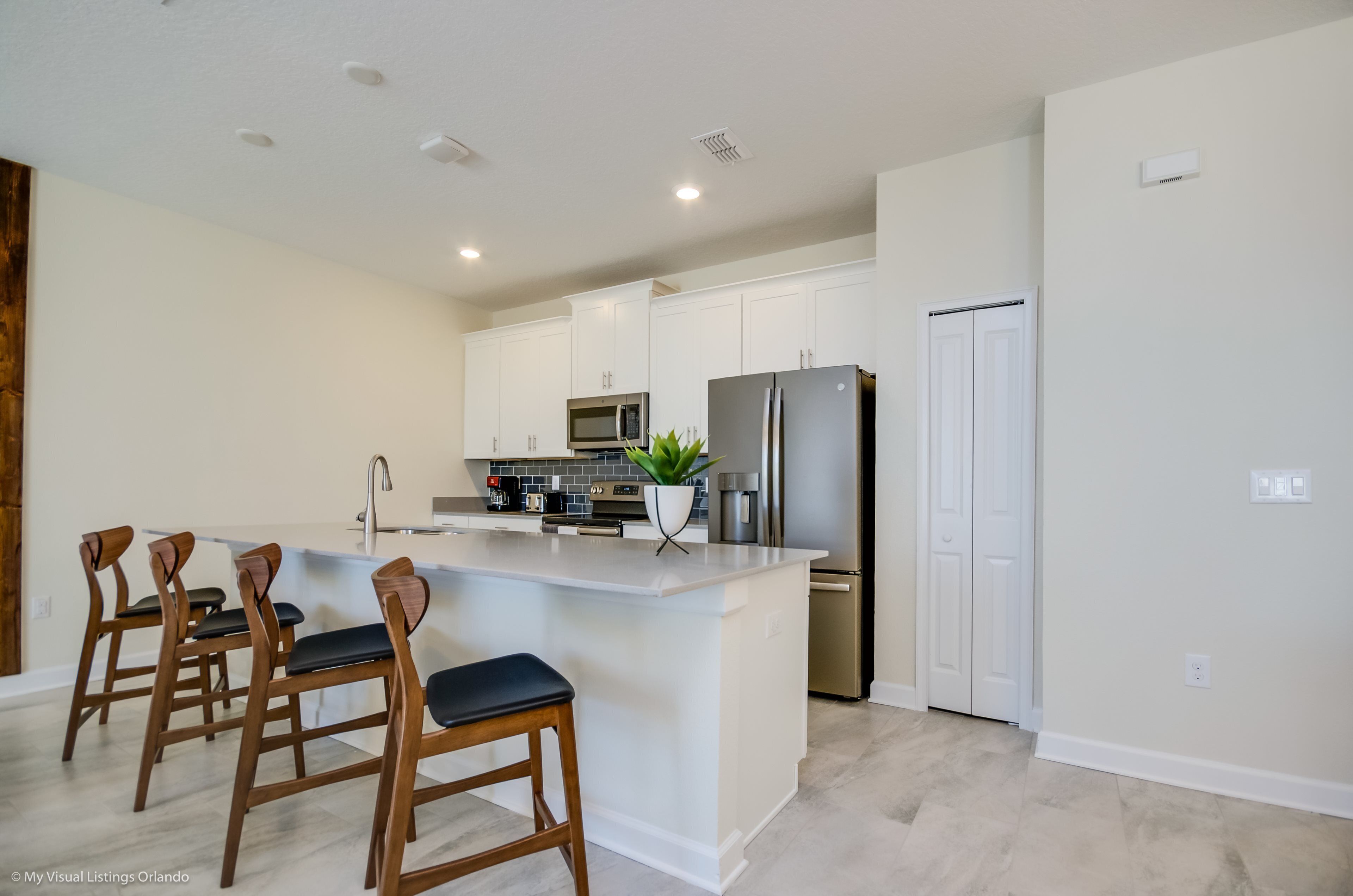 Una cocina moderna con armarios blancos, una isla central, taburetes de bar, un microondas, un refrigerador y un lavamanos.