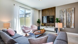 Ein modernes Wohnzimmer mit grauen Sofas, einem Couchtisch und einem Fernseher. Ein großes Fenster mit Vorhängen, eine Pflanze und ein Holzpaneel sind ebenfalls vorhanden.