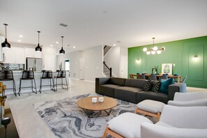 A modern living room with a gray sofa, white armchairs, and a coffee table. - 9BR Villa with Game Room & Theater (Kissimmee)