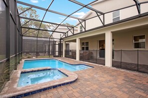 A swimming pool with a glass enclosure, surrounded by a brick patio and a covered seating area. - 9BR Villa with Game Room & Theater (Kissimmee)