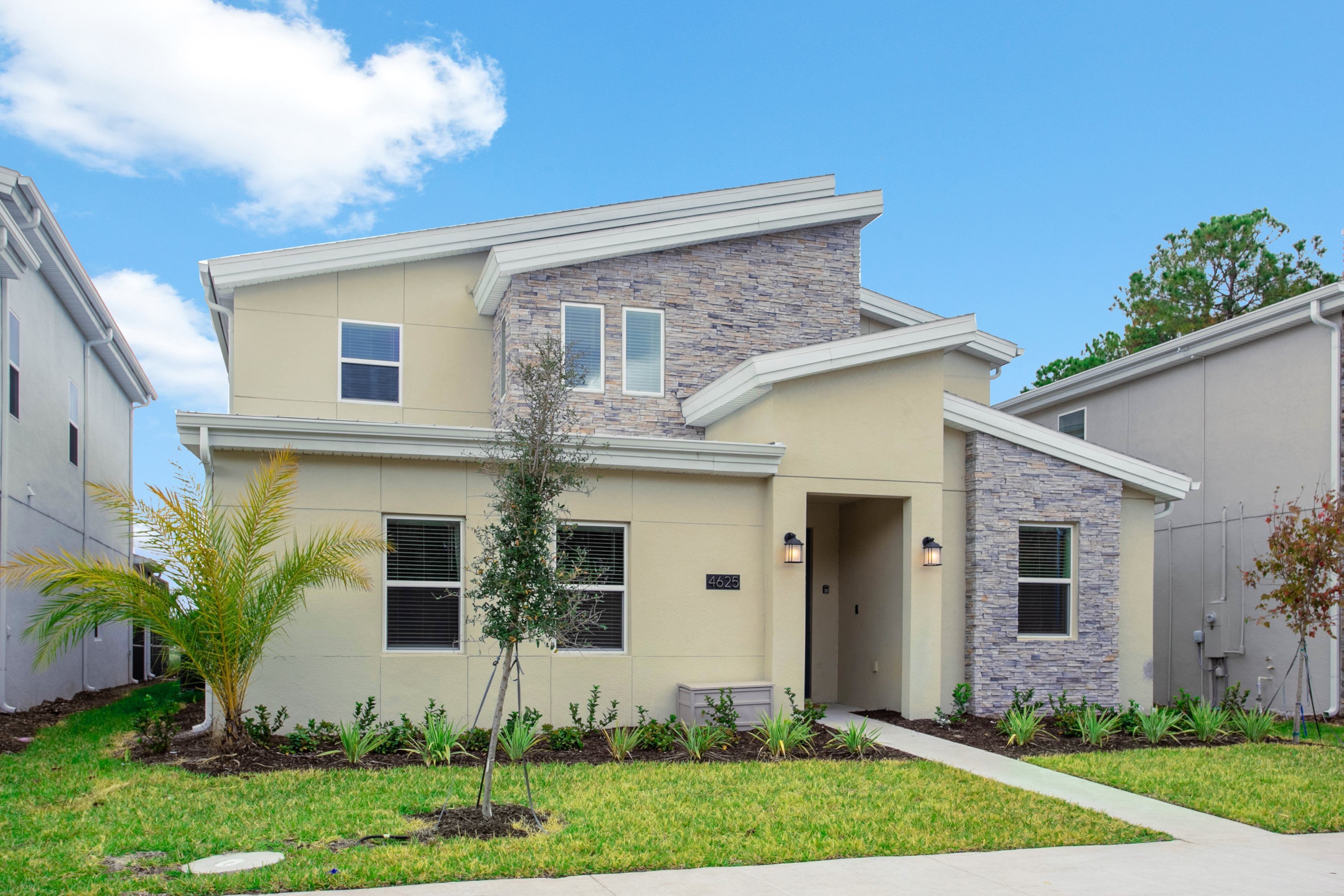 A modern two-story house with a stone facade, a small front yard with landscaping, and a clear blue sky.